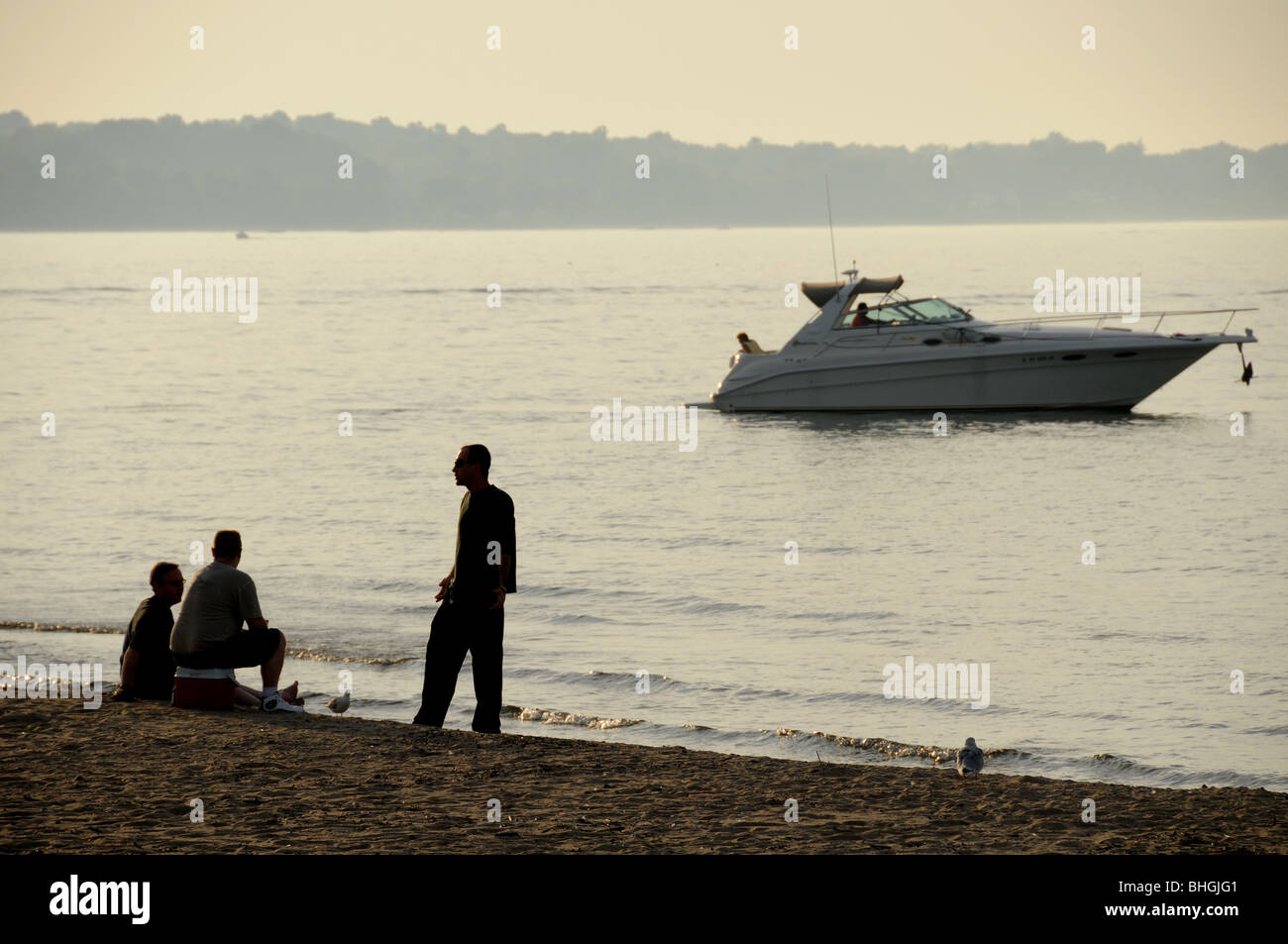 Three men in animated conversation on lake shore. Stock Photo