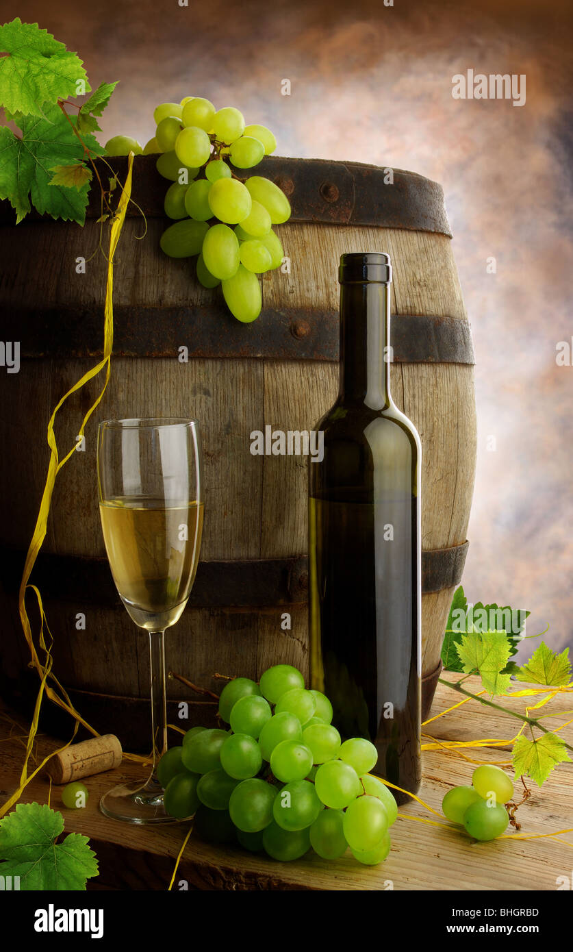 Still life with white wine bottle, glass, old wine barrel, grapes and