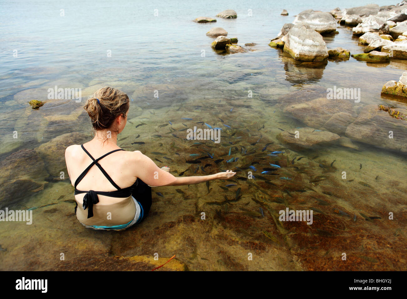 A woman sits with tropical fish in the fresh water lake of lake Malawi near Cape Maclear, Africa Stock Photo