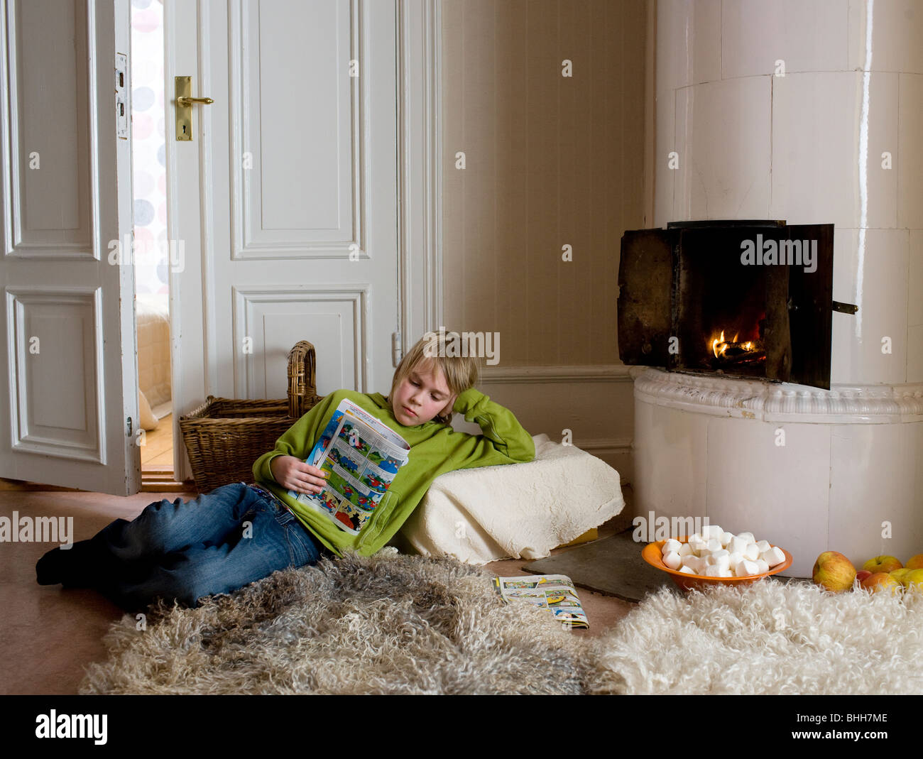 Boy reading by a tiled stove, Sweden. Stock Photo