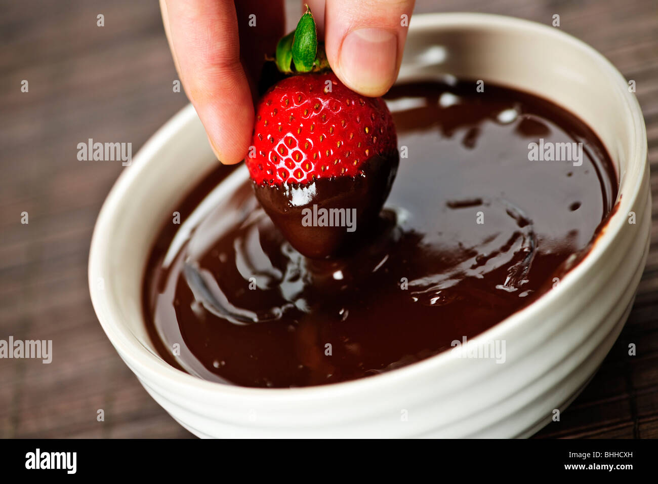 Hand dipping fresh strawberry in melted chocolate Stock Photo