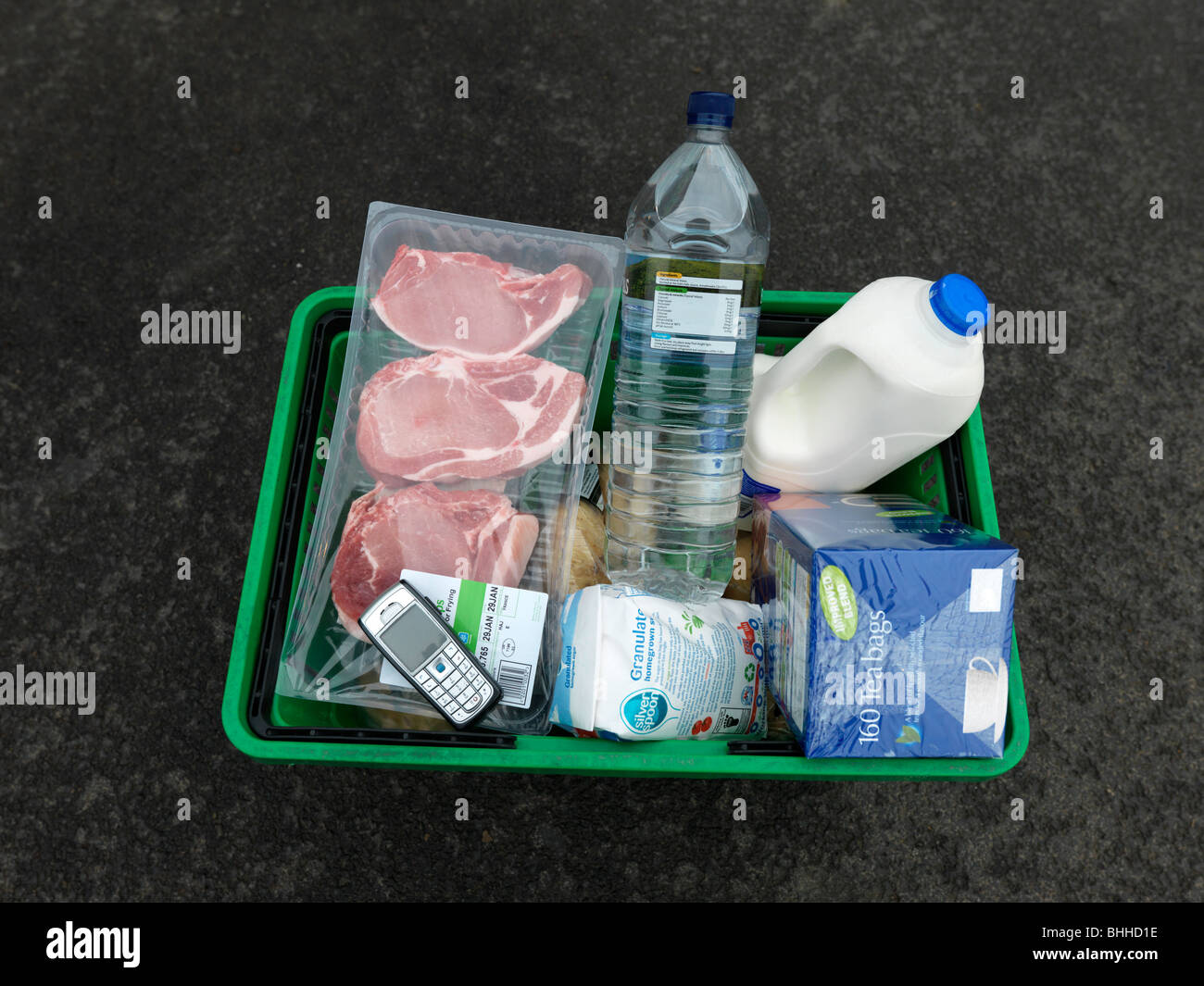 Supermarket Shopping Basket Containing Milk, Meat, Mobile Phone, Sugar, Bottled Water and Tea Stock Photo