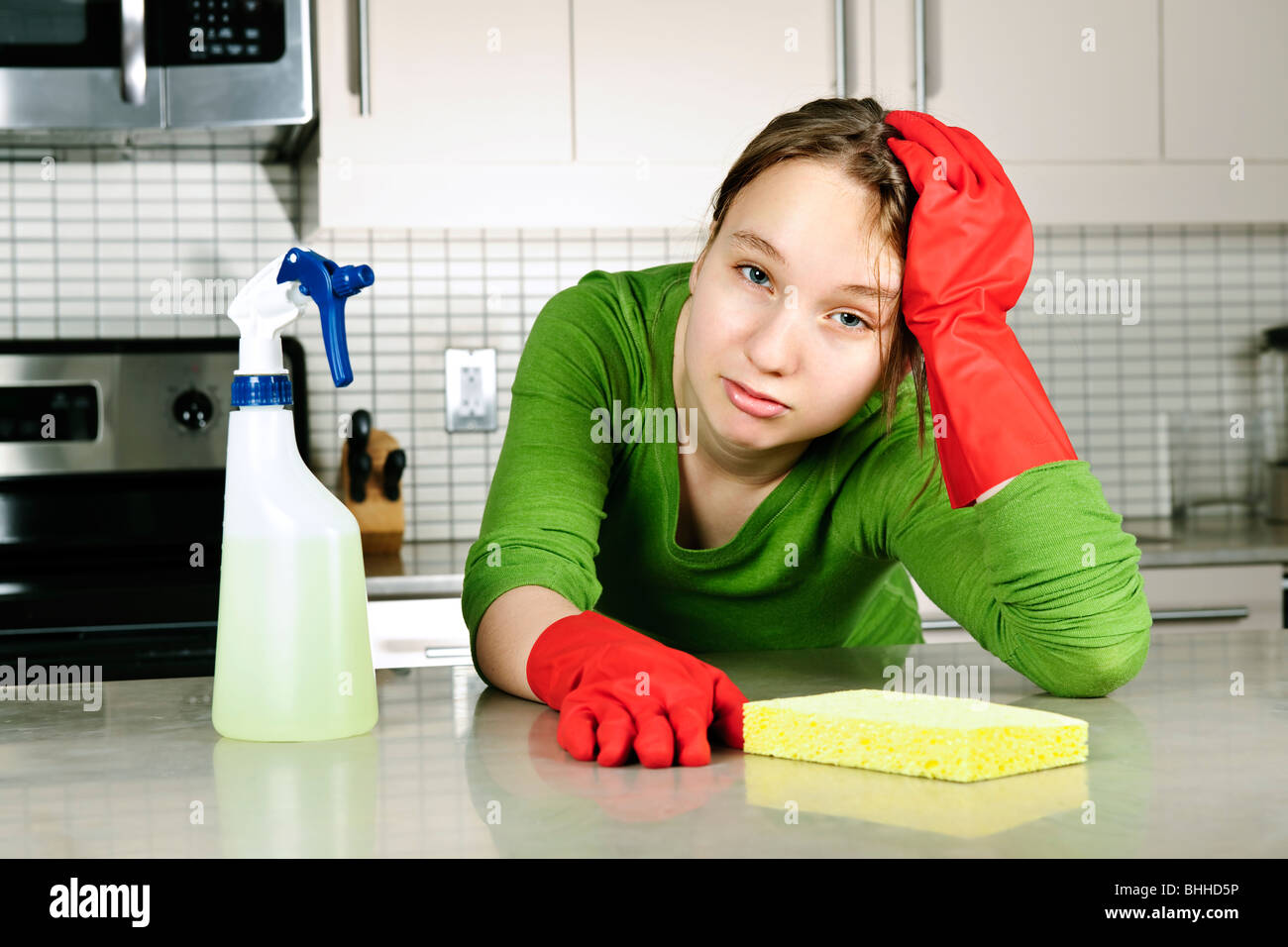 Tired girl doing kitchen cleaning chores with rubber gloves Stock Photo