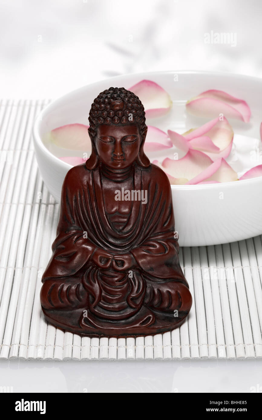 Buddhafigur vor Porzellanschale mit Rosenblaetter Stock Photo