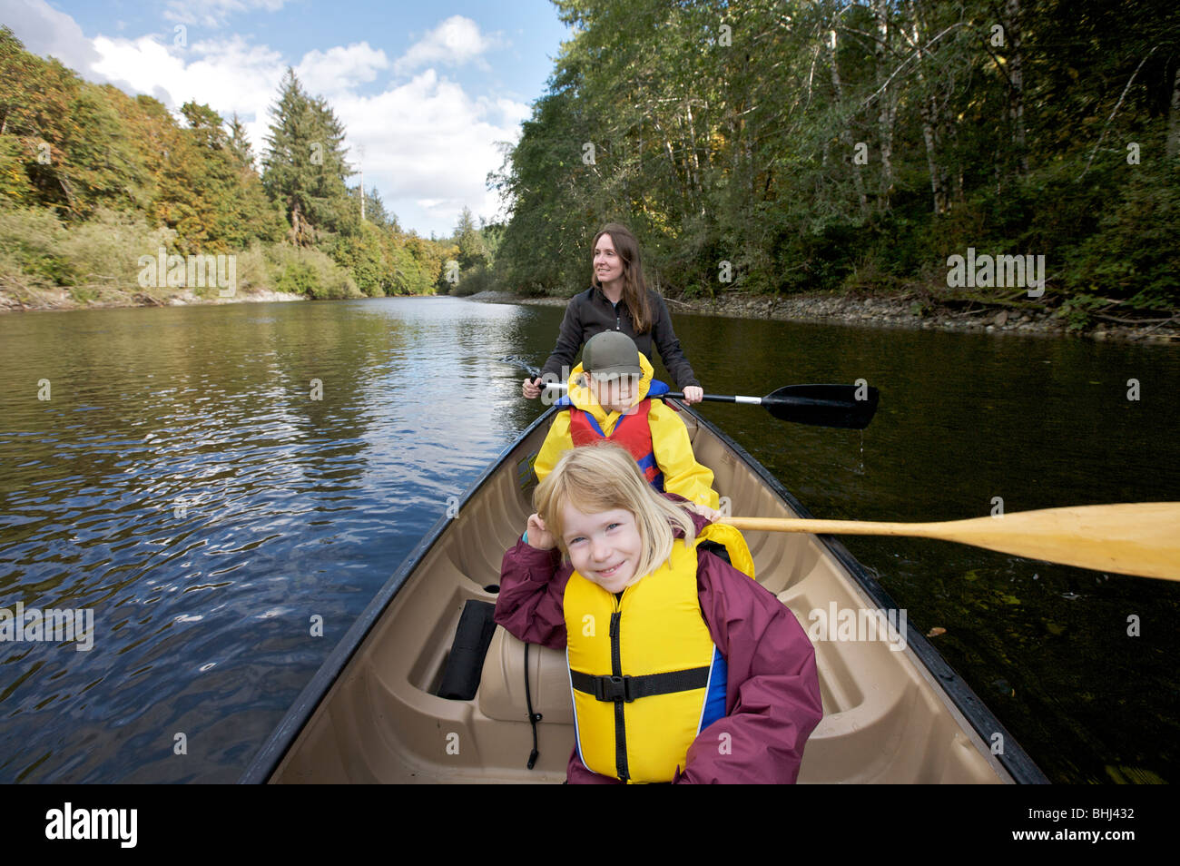 A mother paddles down a river in a canoe with her 2 kids Stock Photo