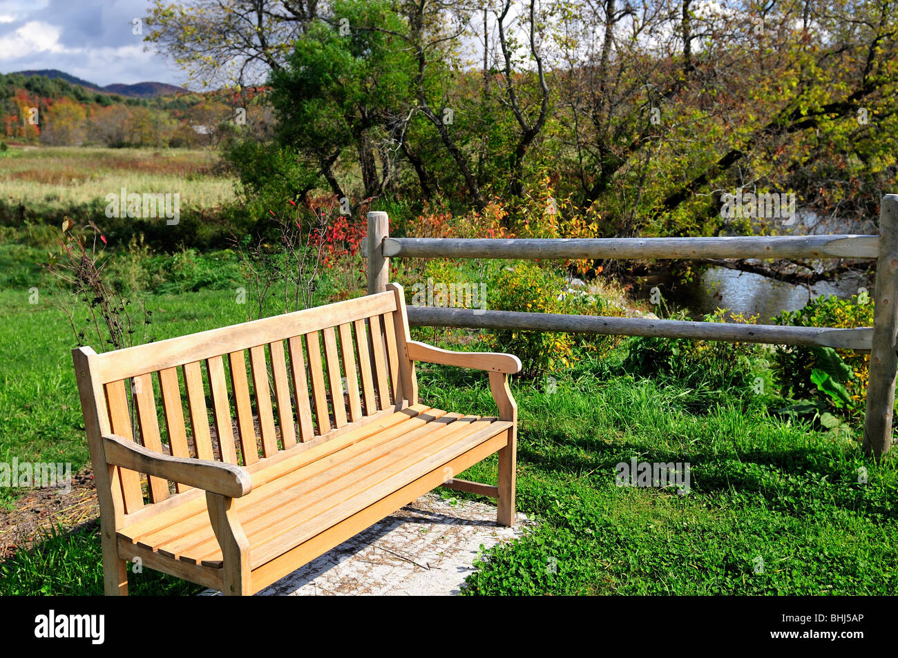 A wooden park bench sits out in nature beside a creek in New Hampshire