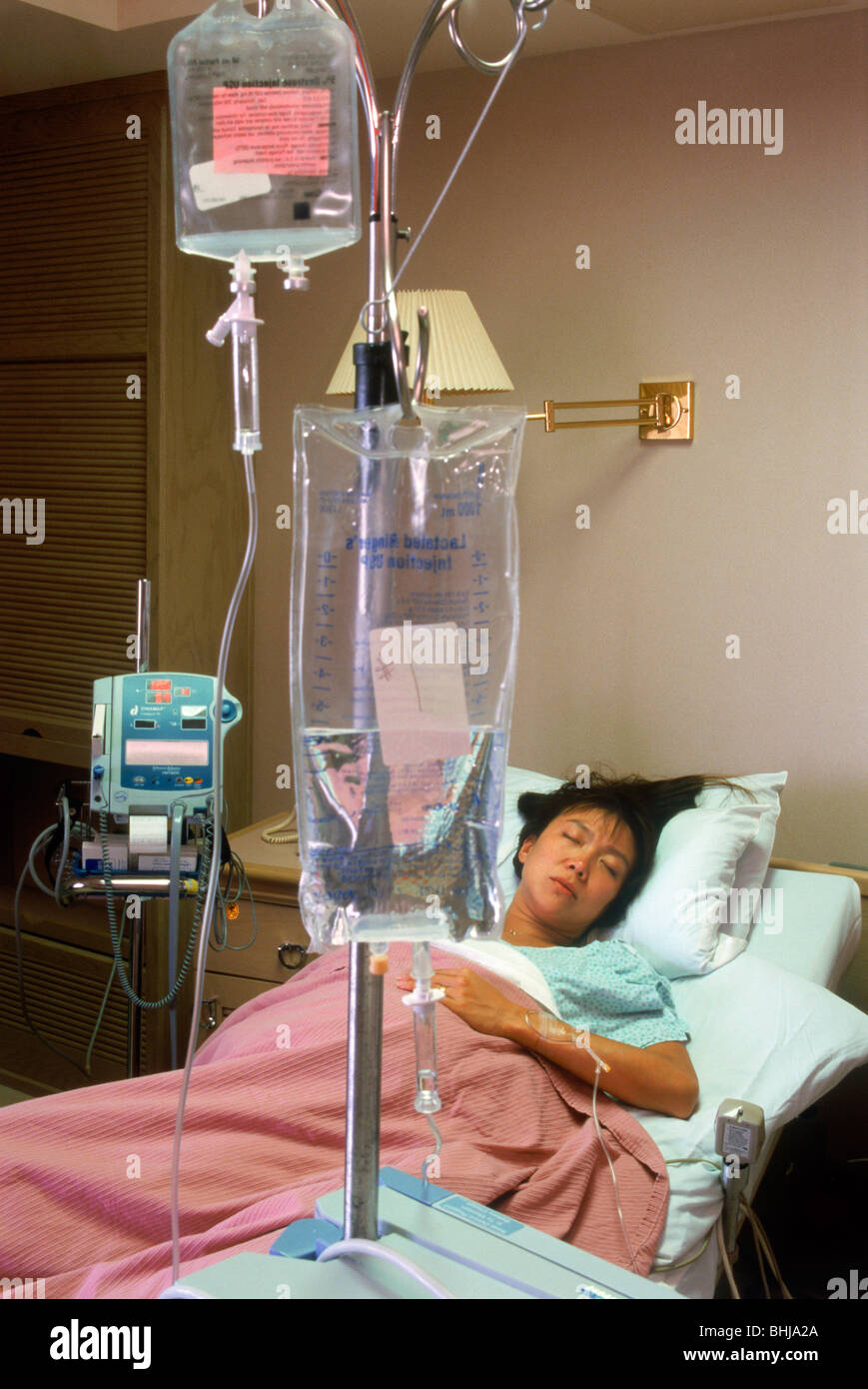 Woman connected to IV tubes in hospital recovery room Stock Photo