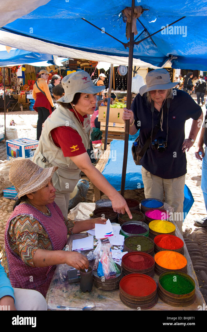 A local woman selling dyes at a market stall in Pisac, Peru. A local guide, Odelia explains to a tourist about the dyes. Stock Photo
