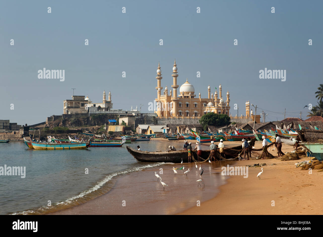 India, Kerala, Kovalam, Vizhinjam village fishermen unloading fishing boats on beach in front of mosque Stock Photo