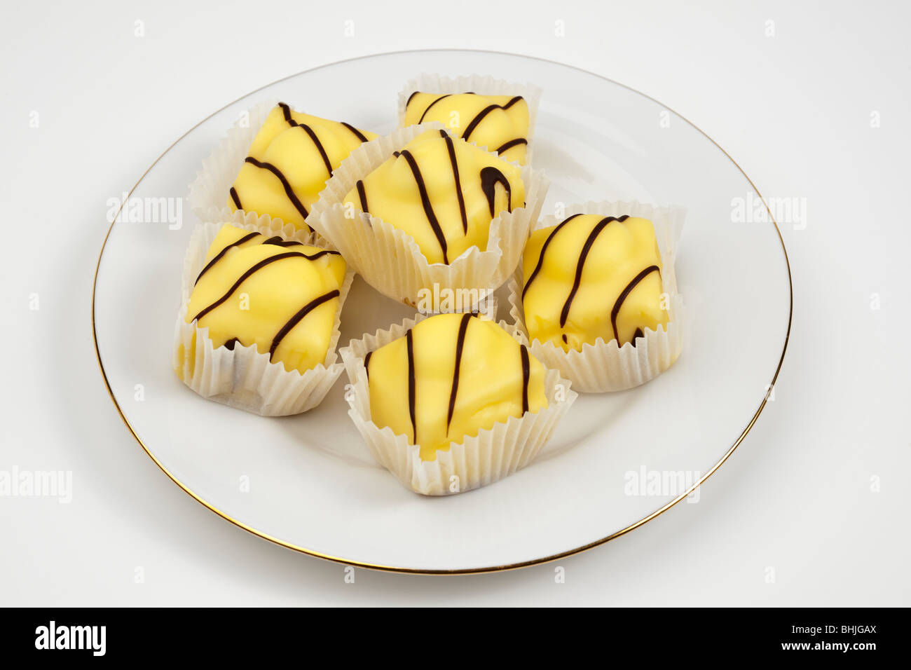 White plate with six Mr Kipling Lemon French Fancies sponge cakes with vanilla topping Stock Photo