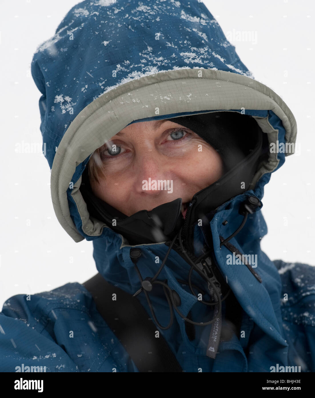 Close up portrait of woman standing in snow smiling at camera with her hood up. Stock Photo