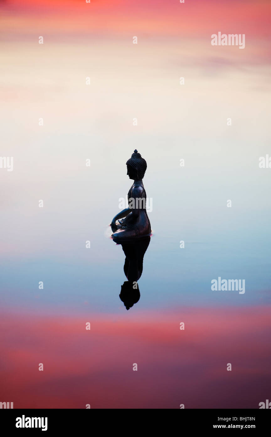 Silhouette of Buddha statue floating on calm still water surface just before sunrise in India Stock Photo