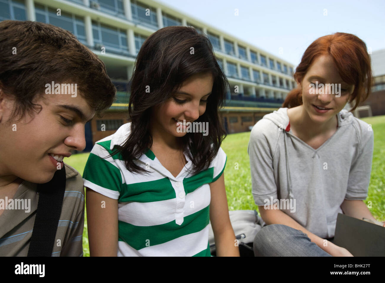 Teenage friends hanging out, sitting together outdoors on school lawn Stock Photo