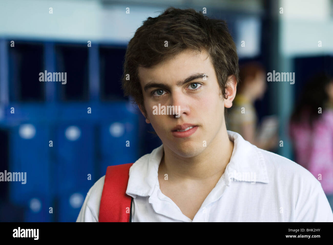 Male high school student standing in hall lined with lockers, portrait