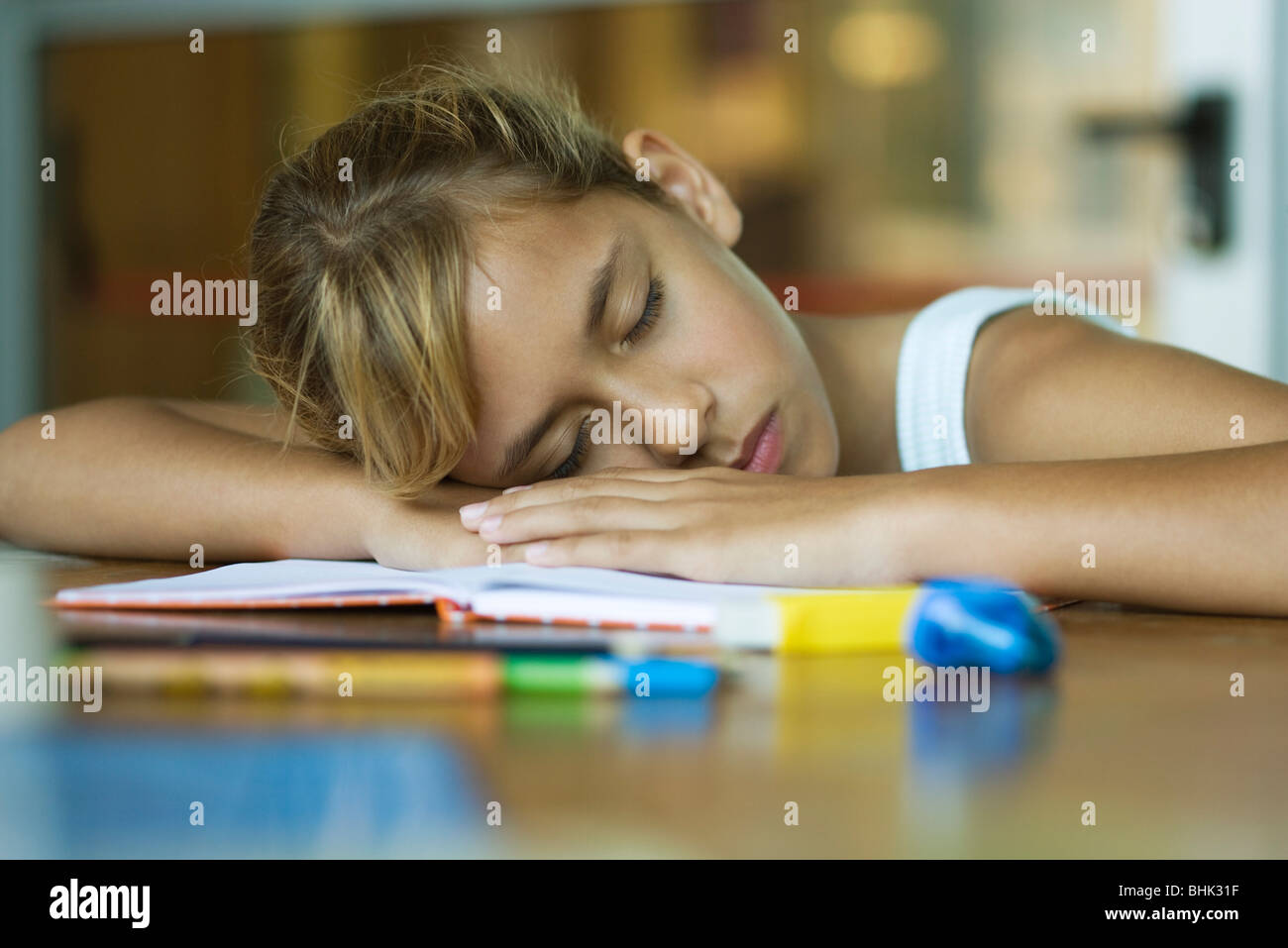 Preteen girl napping, resting head on arms laid across open book Stock Photo