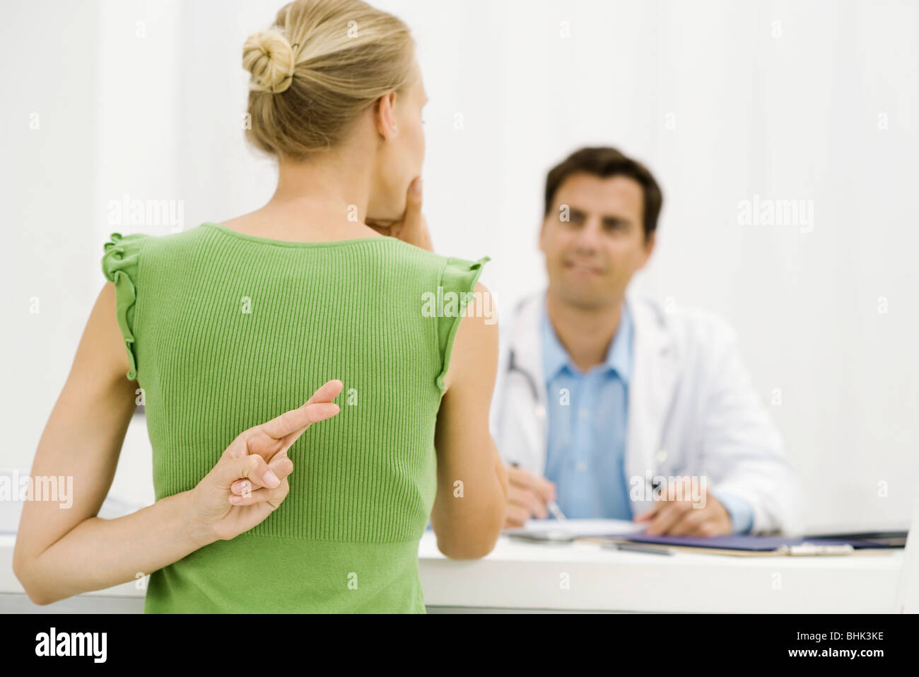 Female patient with hand behind back crossing fingers, speaking with doctor Stock Photo