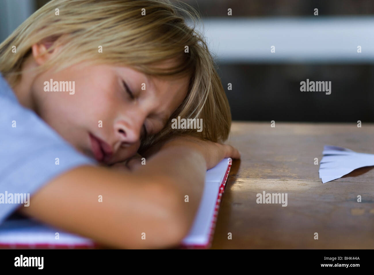 Boy asleep at desk, head resting on arms Stock Photo