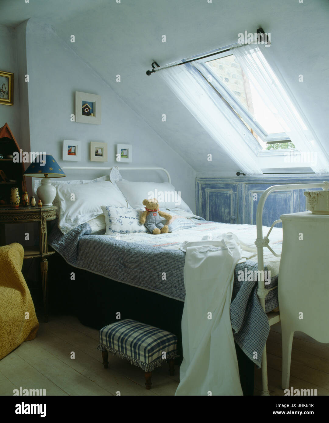 Small stool beside white metal bed with white bedlinen below Velux window in child's attic bedroom Stock Photo