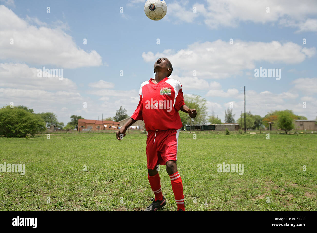 Young black schoolboy playing football or soccer in the village of