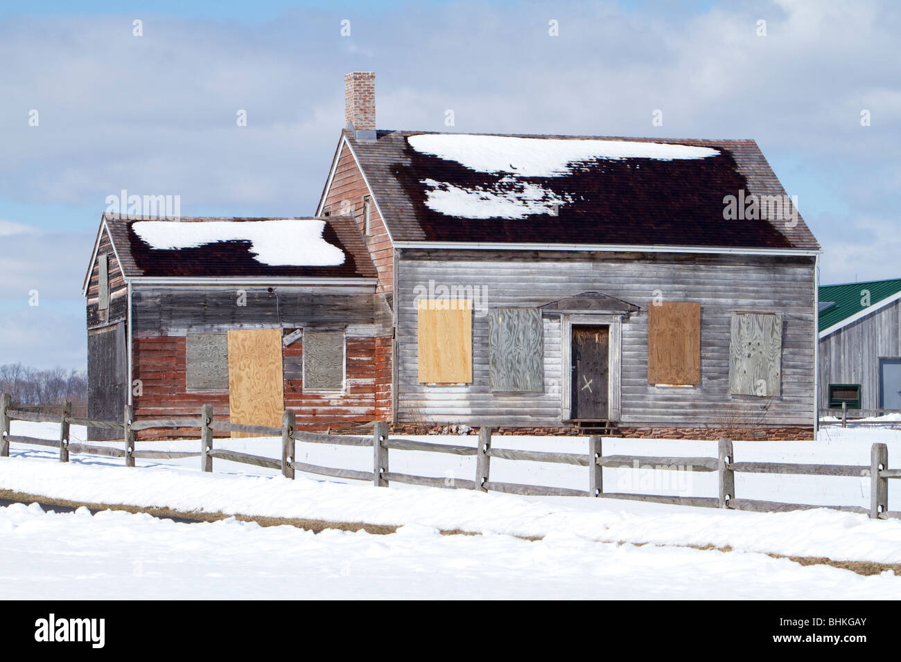 Foreclosed farm house. Vacant and abandoned with windows boarded over. Shot in winter with snow covered ground. Stock Photo