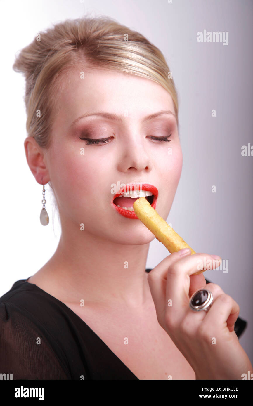 A refined, beautiful young lady eating a chip, French fry, in a seductive manner Stock Photo