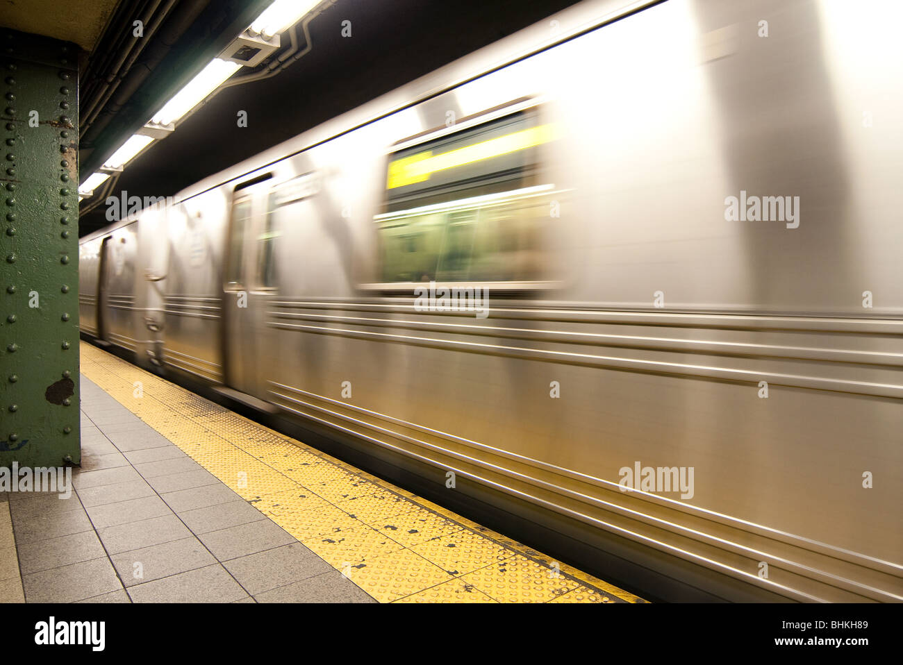 A silver MTA commuter subway train cart in motion blurred riding through a station in New York City next to an empty platform. Stock Photo