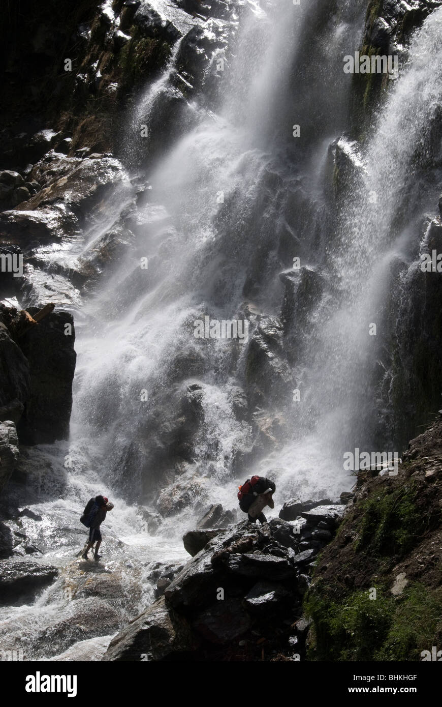 Porters carrying heavy loads across waterfall, near Karte, Annapurna Circuit, Nepal Stock Photo