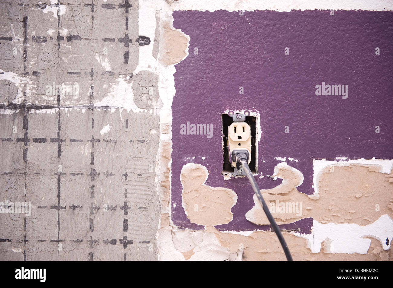 An interior home wall with a 110 volt outlet is being stripped of its tile and prepared for remodeling. Stock Photo