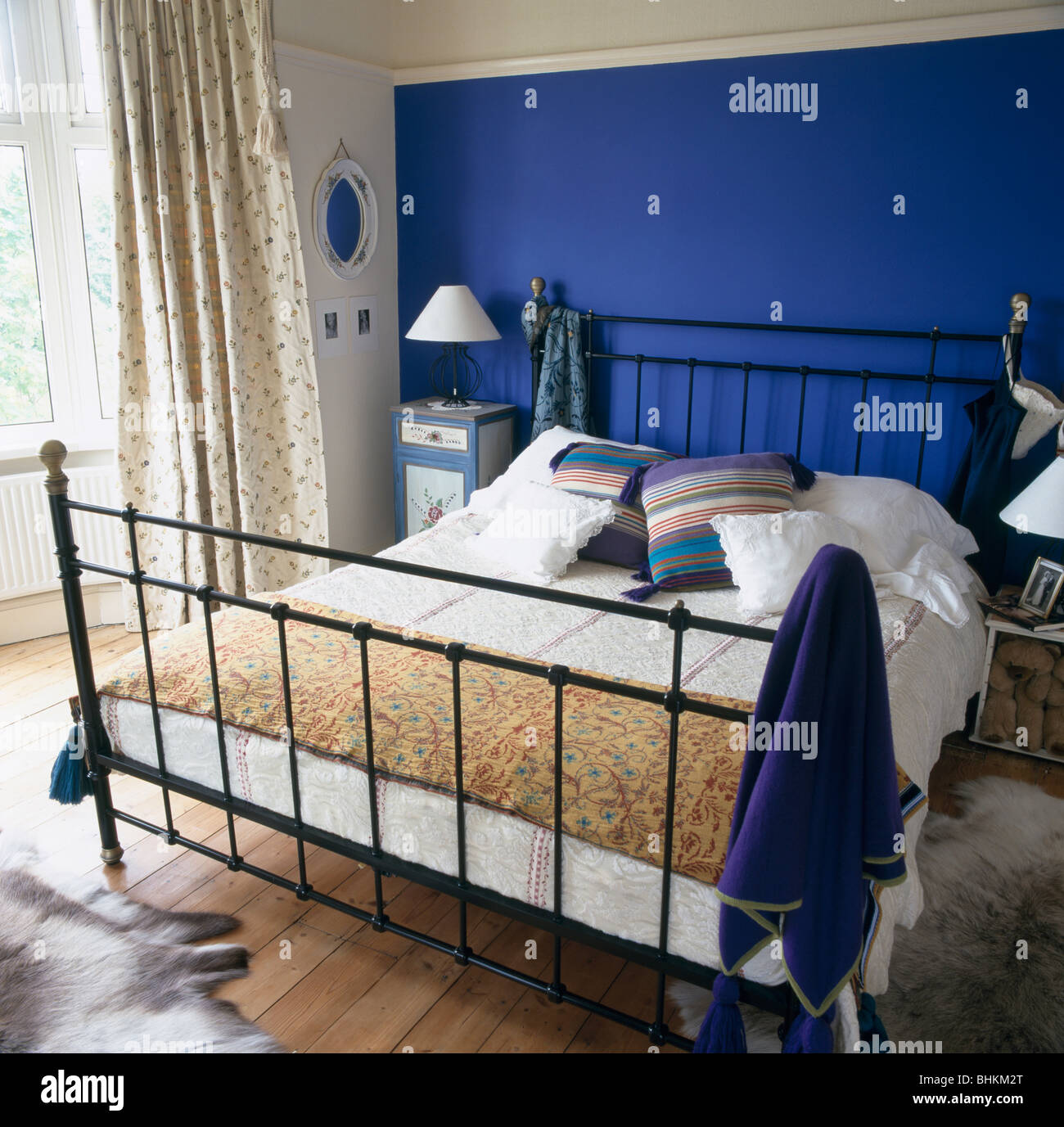 Bright blue wall behind black metal bed with patterned throw in
