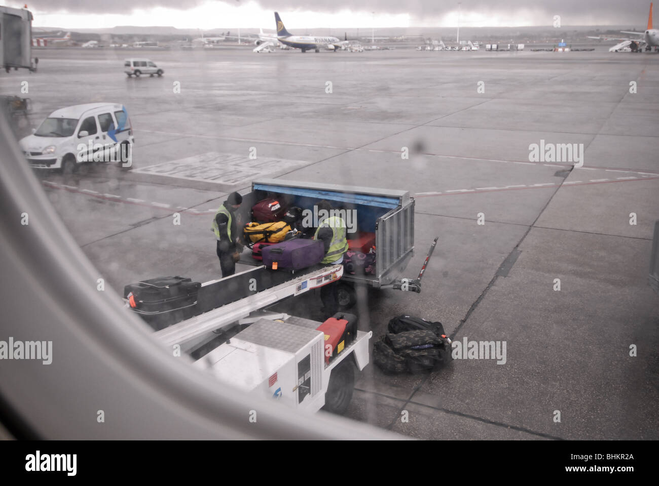 Baggage handlers load luggage onto a passenger plane in the rain Stock