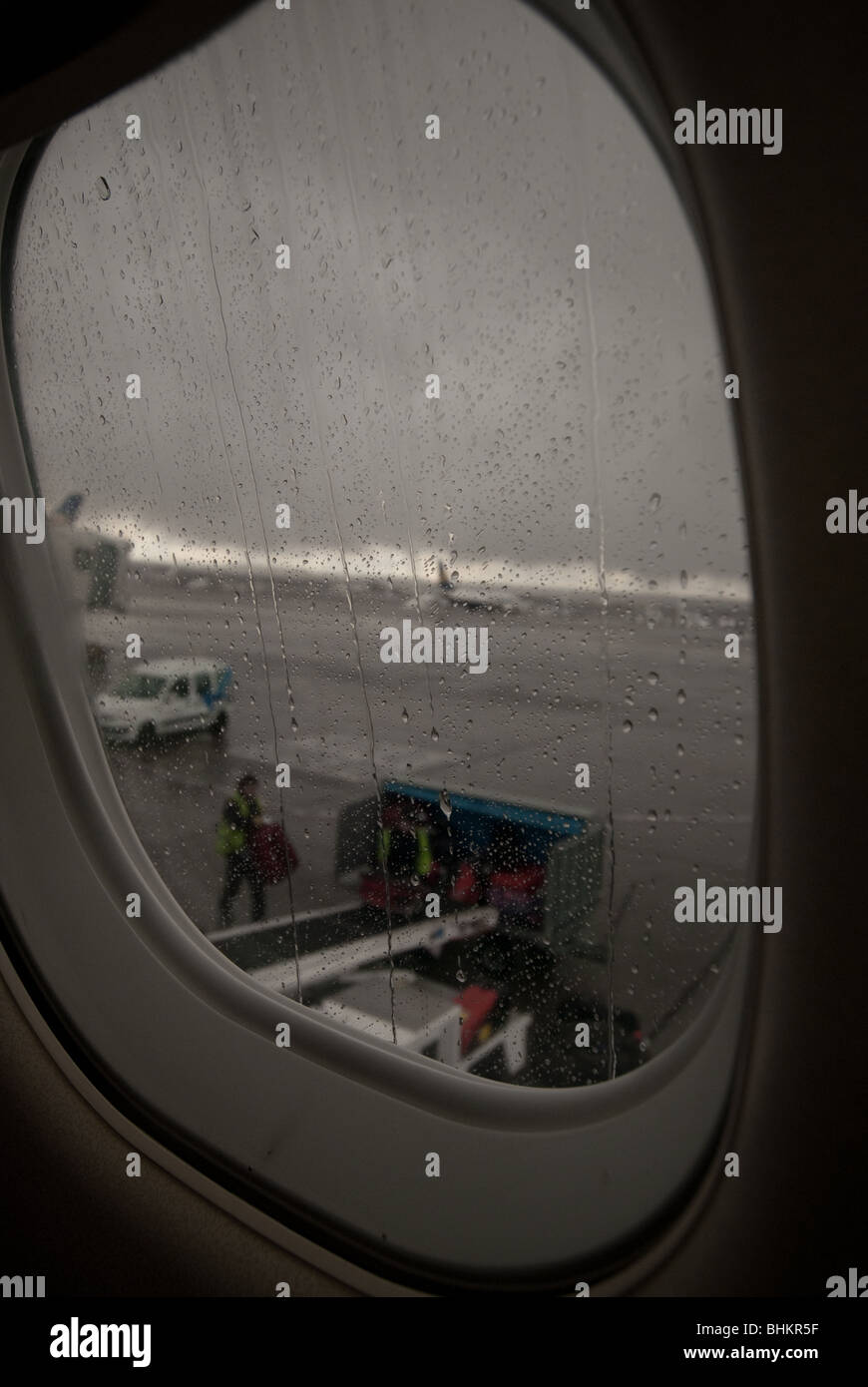 Baggage handlers load luggage onto a passenger plane in the rain. Stock Photo