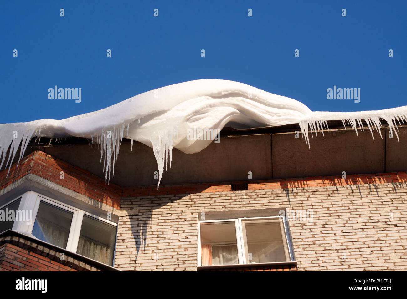Large snowbank and icicles hang from a house roof. Stock Photo