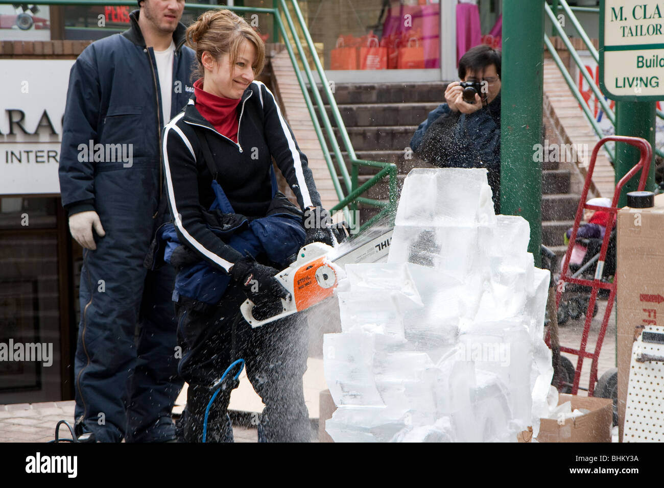 An ice carving artist works on the big block of ice while a photographer took a picture from behind Stock Photo