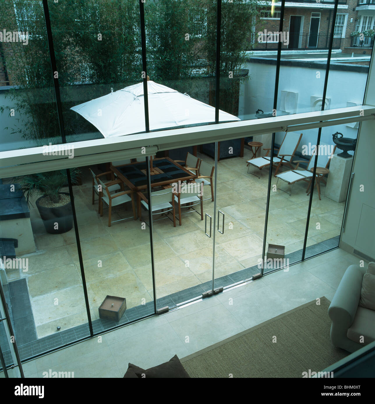 Double-height living-room with view through glass wall of large white  umbrella above furniture in townhouse courtyard Stock Photo - Alamy