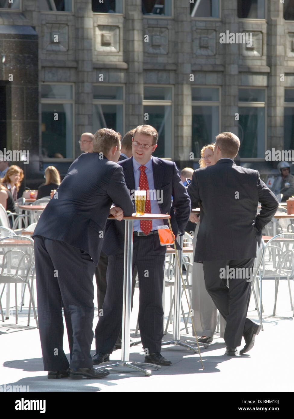 London, Greater London, England. City workers enjoying a drink at the foot of the Swiss Re Tower, also known as the Gherkin. Stock Photo
