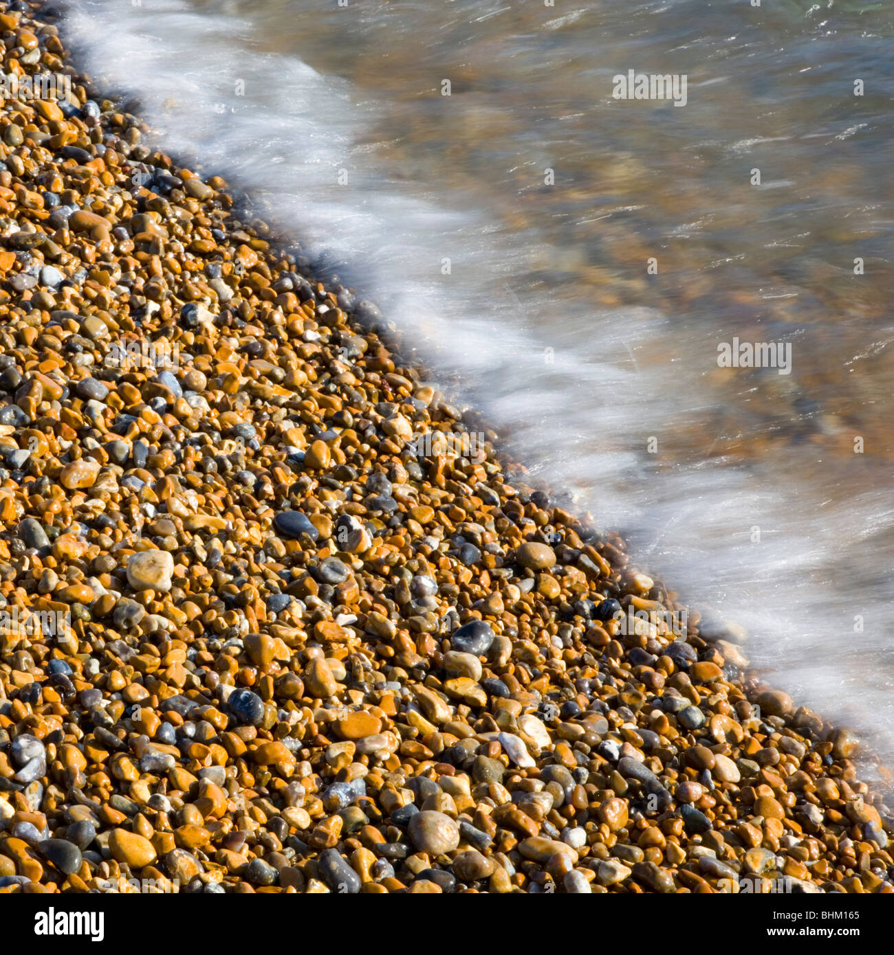 Hastings, East Sussex, England. Sunlit pebbles washed by the incoming tide. Stock Photo