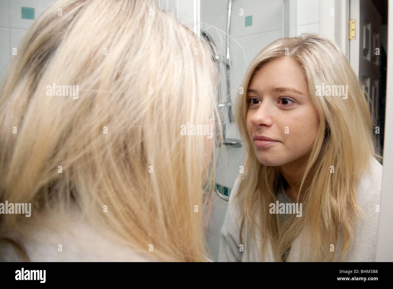 blonde teenage girl looking at her reflection in her bathroom mirror Stock Photo