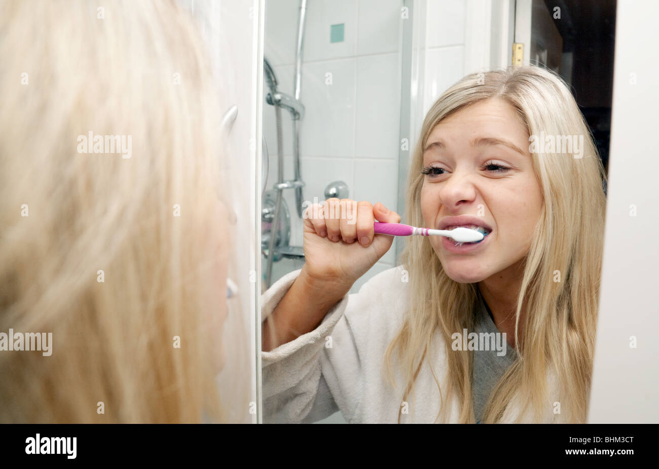 Blonde teenage girl brushing her teeth reflected in her bathroom mirror