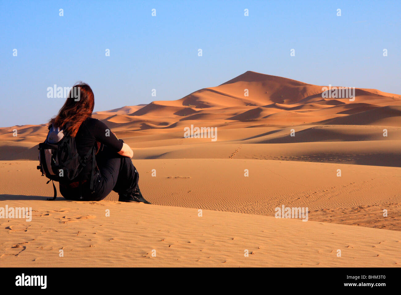 Female tourists looks out across the Erg Chebbi snad dunes in the Sahara Desert near Merzouga, Morocco Stock Photo