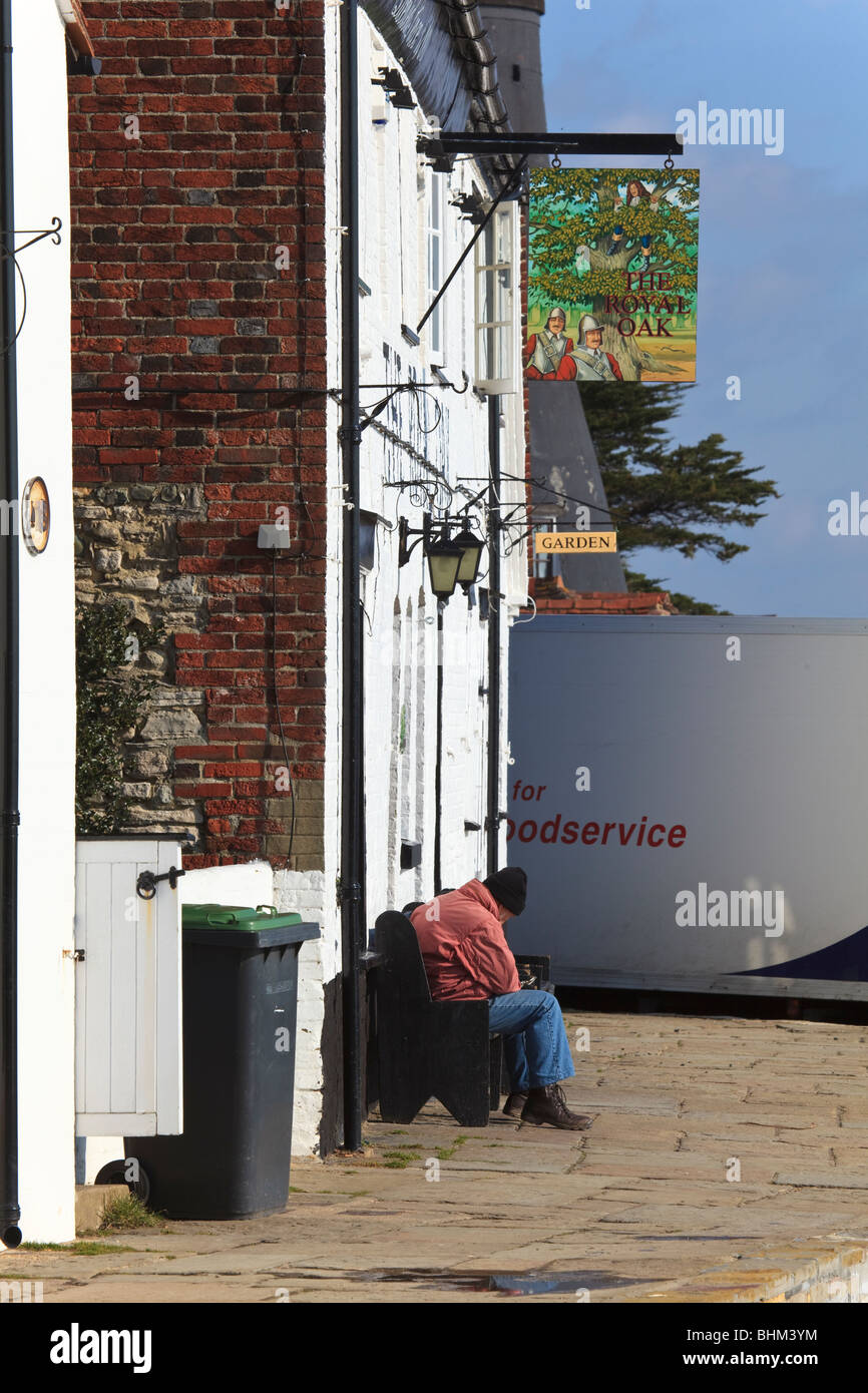 An Elderly man sits outside 'The Royal Oak' pub on the waterfront at Langstone, in the winter sunshine, Hampshire, Uk Stock Photo