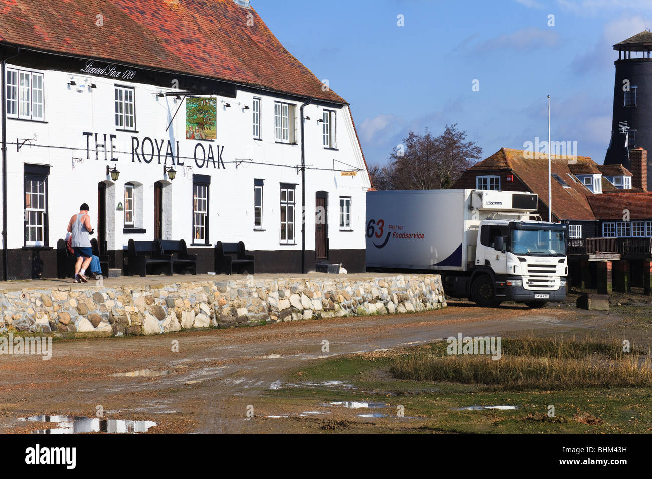 A van delivers to the Royal Oak at Langstone at low tide, a runner on the 'Solent Way' passes, Hampshire, UK Stock Photo