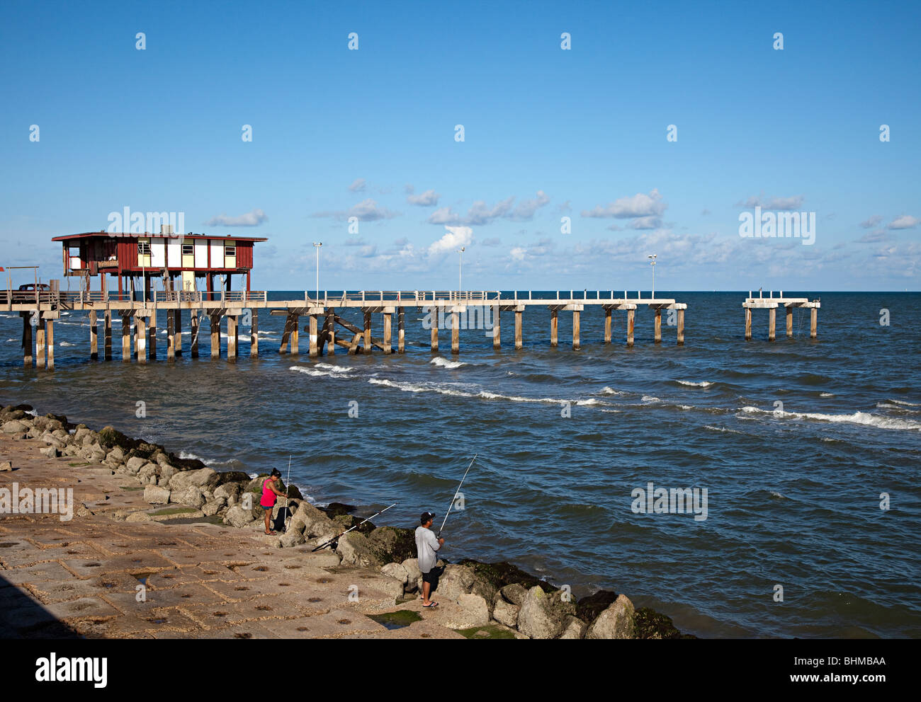 Two people fishing on sea front beside ruined pier Galveston Texas USA Stock Photo