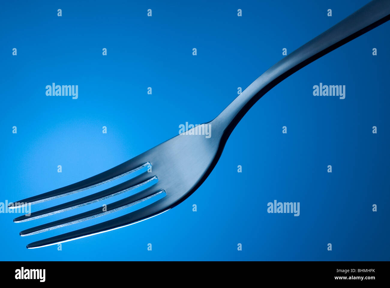Stainless steel fork against a blue background. Stock Photo