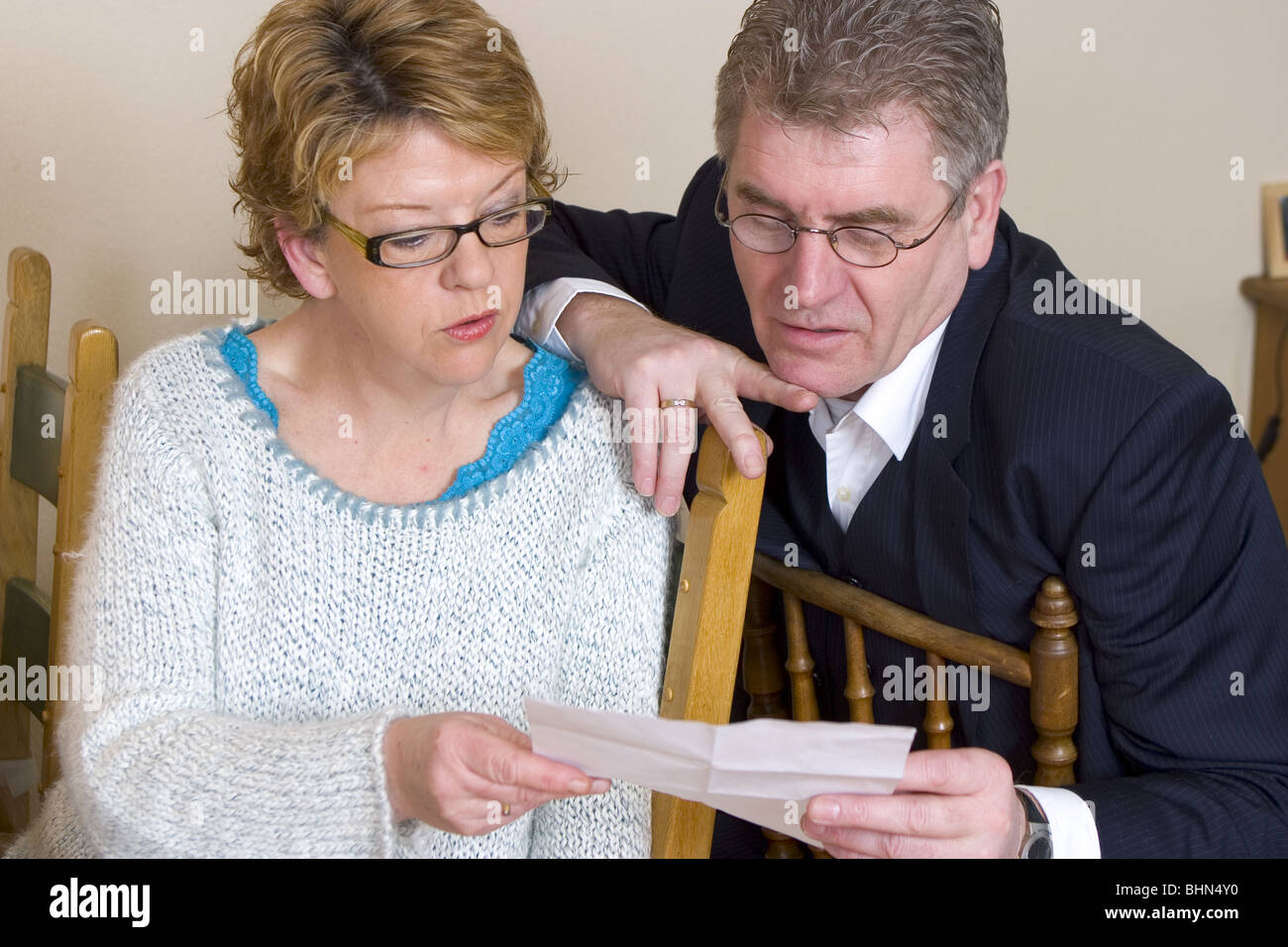 Spouses reading a letter and looking worried at the message in their hands. Stock Photo