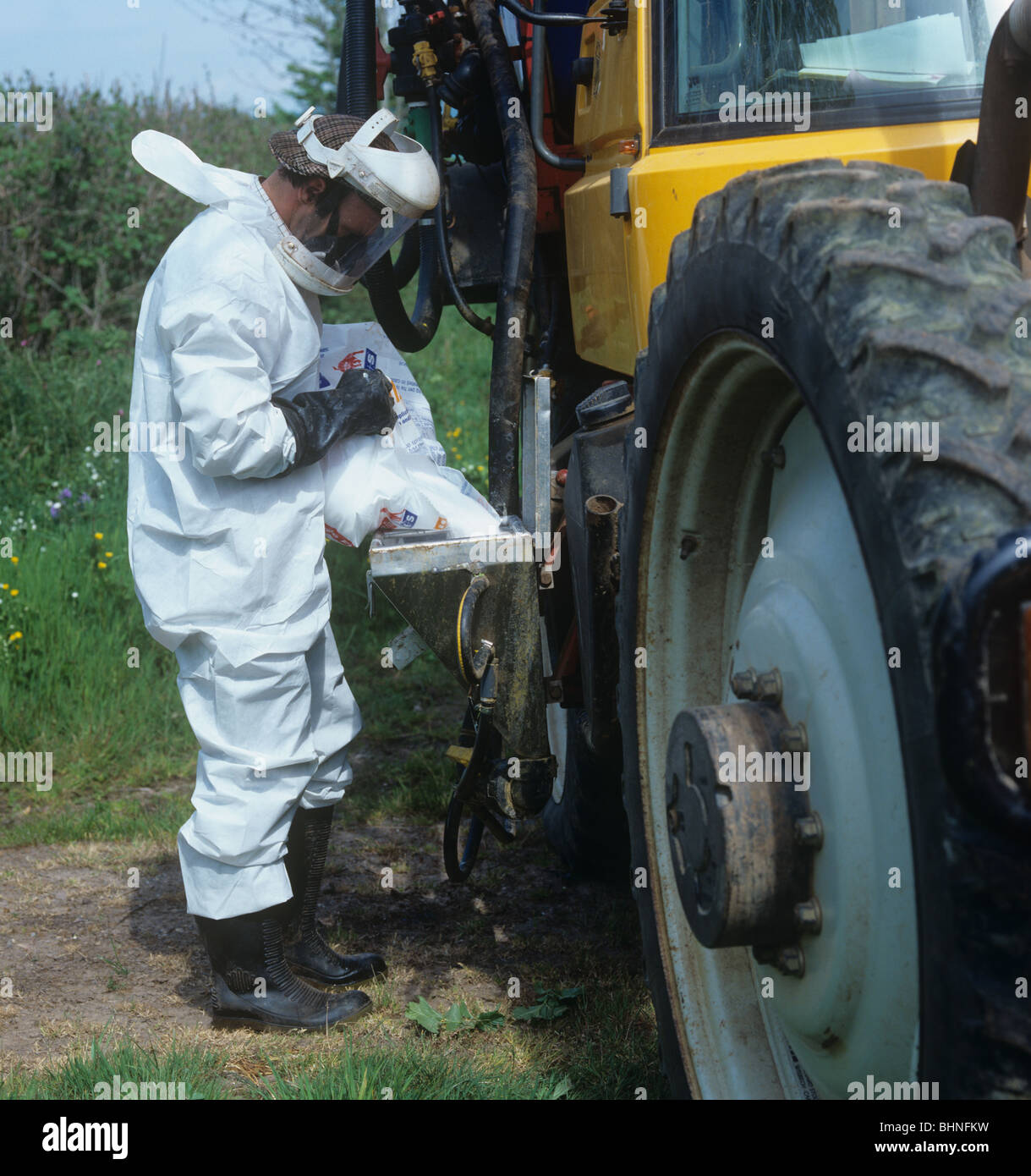 Worker wearing full protective gear filling tank on Gem 2000 sprayer mounted on Fastrac tractor Stock Photo