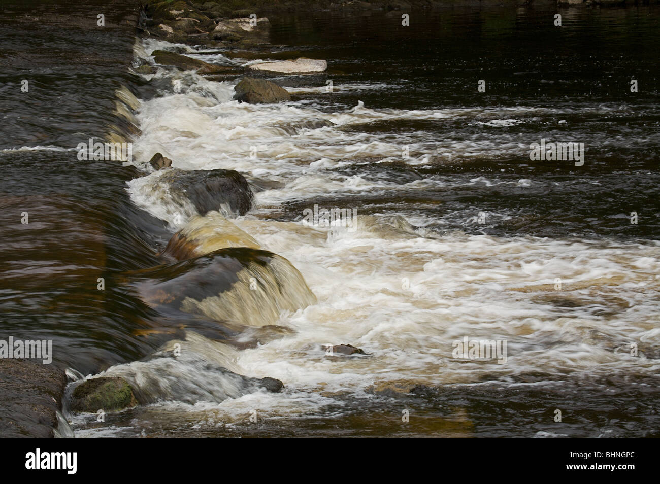 Silt-laden water rushing over a weir on the River Stour Blandford Dorset  England UK Stock Photo - Alamy