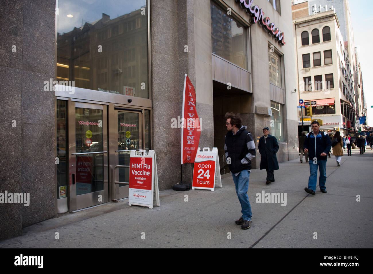 Pedestrians pass a sign saying H1N1 flu shots available outside a Walgreen 's pharmacy in the Murray Hill neighborhood of NY Stock Photo