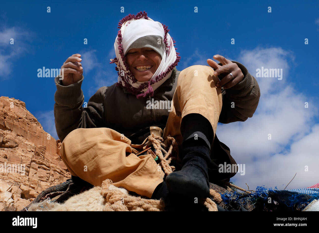 Young nomadic Bedouin boy poses to camera from a high perch atop of a camel back Stock Photo