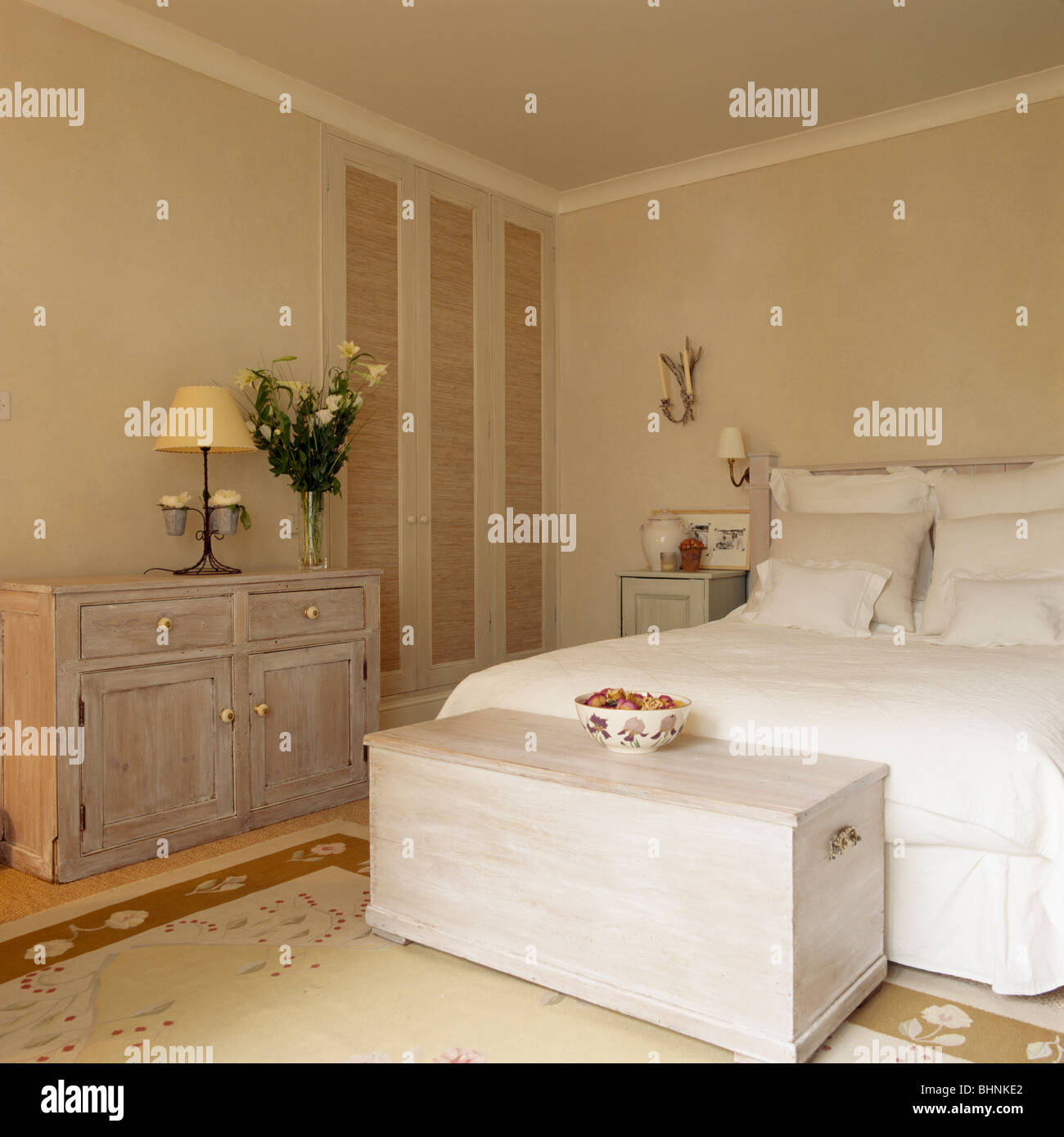 Limed wooden chest below bed with white quilt and pillows in white