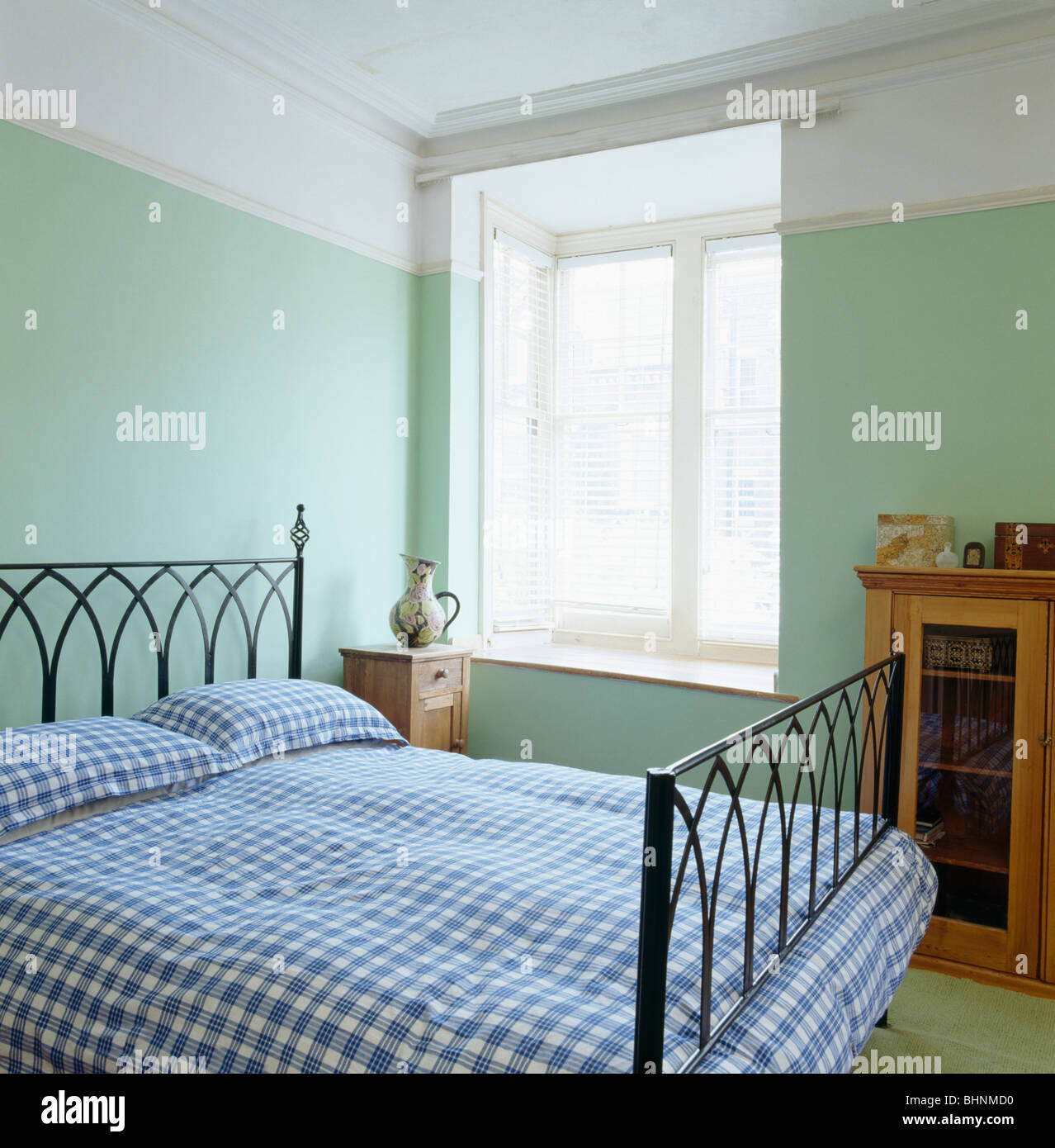 Blue checked quilt and pillows on wrought iron bed in pastel green